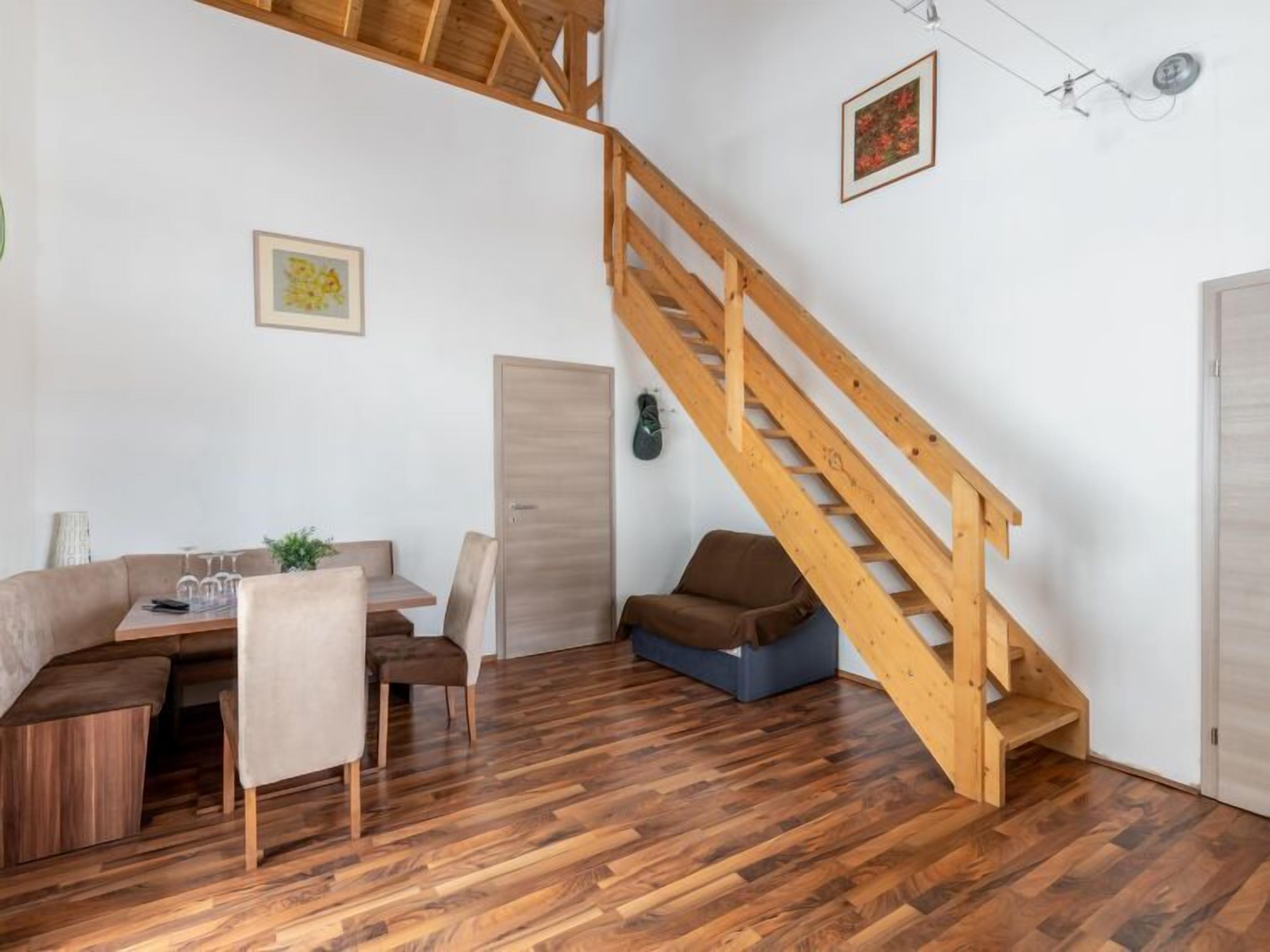 Una habitación con una escalera de madera, una zona de comedor con una mesa y sillas, y un sofá.