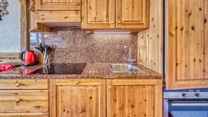 A kitchen with wooden cabinets, a granite countertop, a sink, and a stove. - Belleville Caron 1 - 1213 by Interhome (Les Menuires)