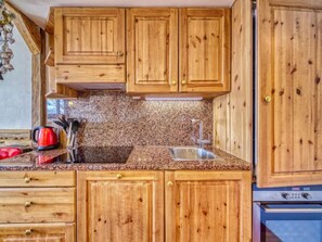 A kitchen with wooden cabinets, a granite countertop, a sink, and a stove. - Belleville Caron 1 - 1213 by Interhome (Les Menuires)