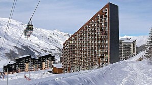 A modern ski resort with a large building featuring a grid-like facade, a ski lift, and snow-covered mountains in the background. - Belleville Caron 1 - 1213 by Interhome (Les Menuires)