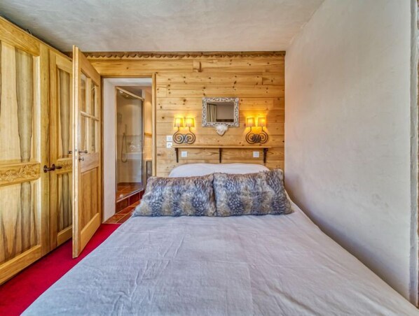 A wooden room with a bed, a wooden wardrobe, and a mirror on the wall.