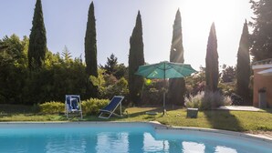 A swimming pool with two lounge chairs and an umbrella, surrounded by tall trees and a well-maintained lawn. - Un petit coin de paradis by Interhome (Châteaurenard)