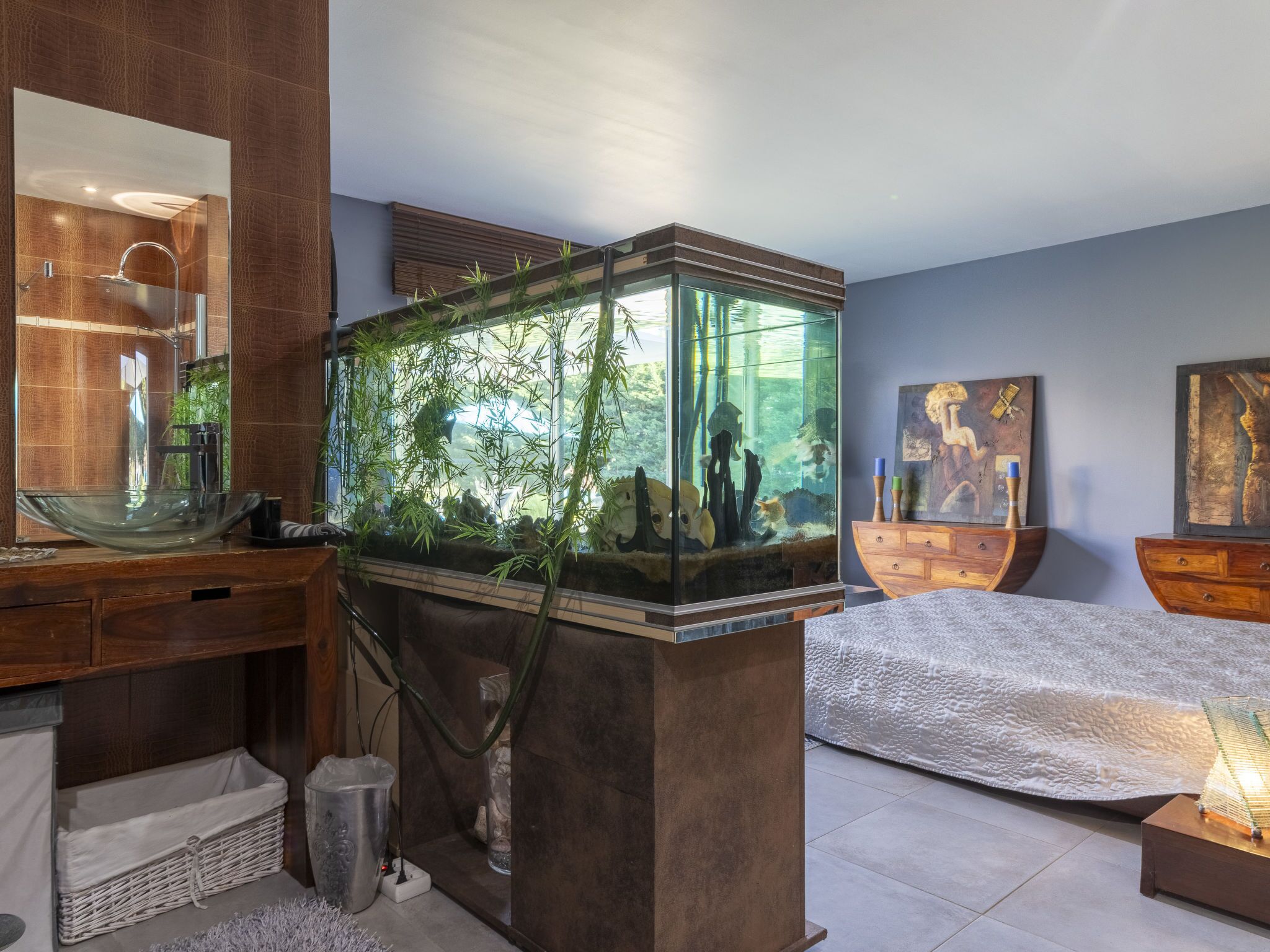 A modern bathroom with a large glass fish tank, wooden vanity, and artwork on the walls.