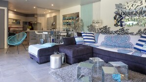 A modern living room with a sectional sofa, a blue chair, and a kitchen in the background. - Un petit coin de paradis by Interhome (Châteaurenard)