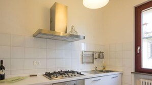 Una cucina compatta con mobili bianchi, un fornello a gas, una cappa in acciaio inossidabile, un lavello e una finestra vista esterna.