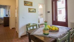 Un'area pranzo con un tavolo apparecchiato per due, un vaso verde e un cesto di limoni. Si notano due sedie, un tavolo di legno e una porta con una finestra.