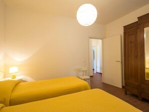 A room with two beds, a wooden wardrobe, a lamp, and a door leading to another room.