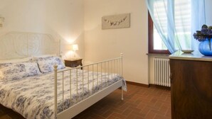 Una camera da letto con un letto singolo, un comodino, una lampada, un termosifone e una finestra con tende.