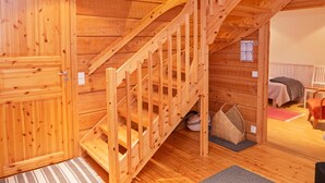 A wooden staircase leading to an upper level, a bed with a blanket, and a small table with a chair.
