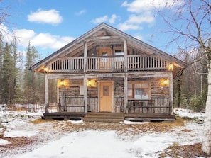 A rustic log cabin with a balcony, a front door, and a sign that reads 'SUOPURSU'.
