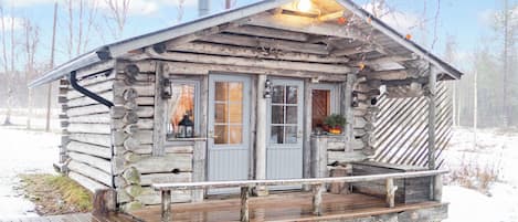 A rustic log cabin with a porch, a chimney, and a deck.