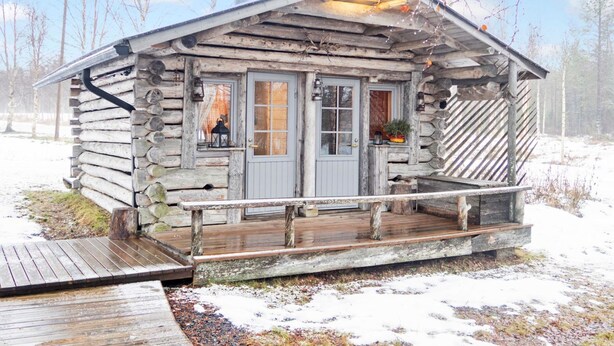 A rustic log cabin with a wooden deck, a front porch, and a chimney.