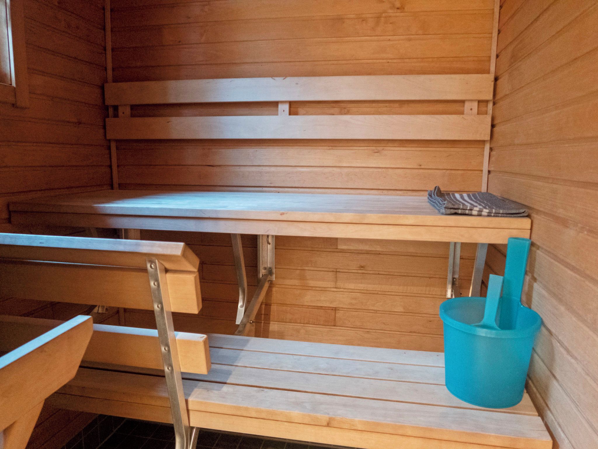 A sauna room with wooden benches and a blue bucket.