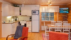 A compact kitchen with white cabinets, a microwave, a stove, and a refrigerator. There is a dining area with a wooden table and white chairs.