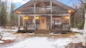 A rustic log cabin with a balcony, a wooden door, and a sign reading "SUOPURSU".