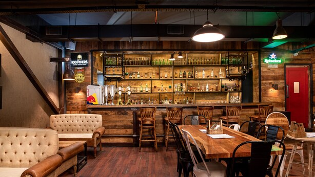 A bar area with wooden furniture, a variety of bottles, and a neon sign.