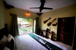 A bedroom with a bed, a ceiling fan, a window with curtains, and a view of the outdoors. - Regenta Resort Aranyaani (Kurai)