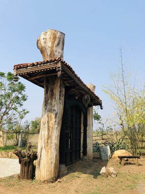 A rustic wooden structure with a tiled roof and a large tree trunk supporting it. - Regenta Resort Aranyaani (Kurai)