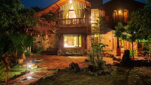 A rustic stone building with a balcony, a large window, and a clock tower. - Regenta Resort Aranyaani (Kurai)
