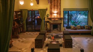A cozy living room with a fireplace, green curtains, and a checkered floor. - Regenta Resort Aranyaani (Kurai)