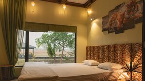 A bedroom with a large bed, a window with a view of trees, and a tiger-themed headboard. - Regenta Resort Aranyaani (Kurai)