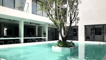 A modern indoor pool area with clear water, surrounded by a covered seating area with chairs and tables.
