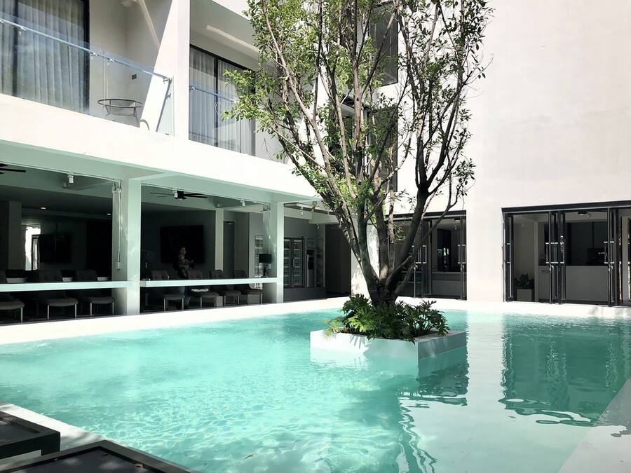 A modern indoor pool area with clear water, surrounded by a covered seating area with chairs and tables.