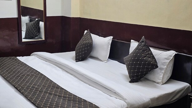 A neatly made bed with a patterned bedspread, a headboard with a dark finish, and a mirror on the wall.
