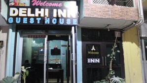 The entrance to Delhi Inn Guest House with a signboard, glass doors, and potted plants outside.
