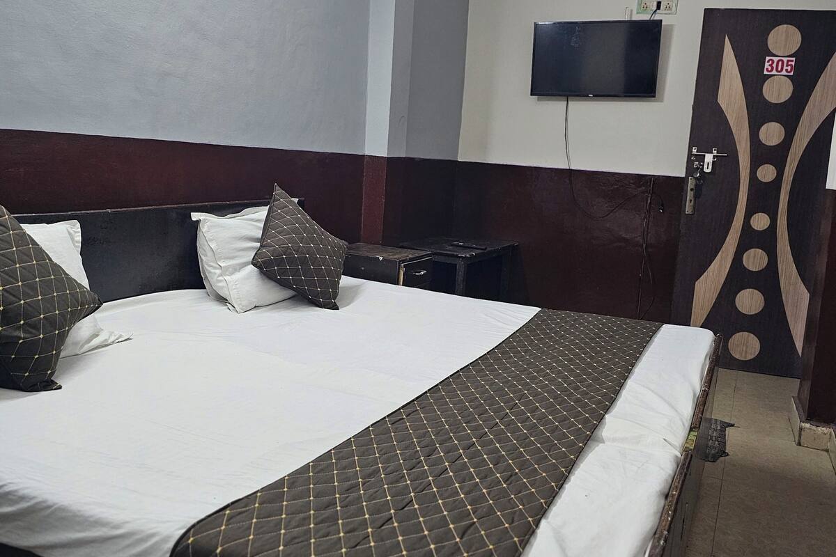 A hotel room with a bed, a ceiling fan, a TV mounted on the wall, and a door with a decorative panel.