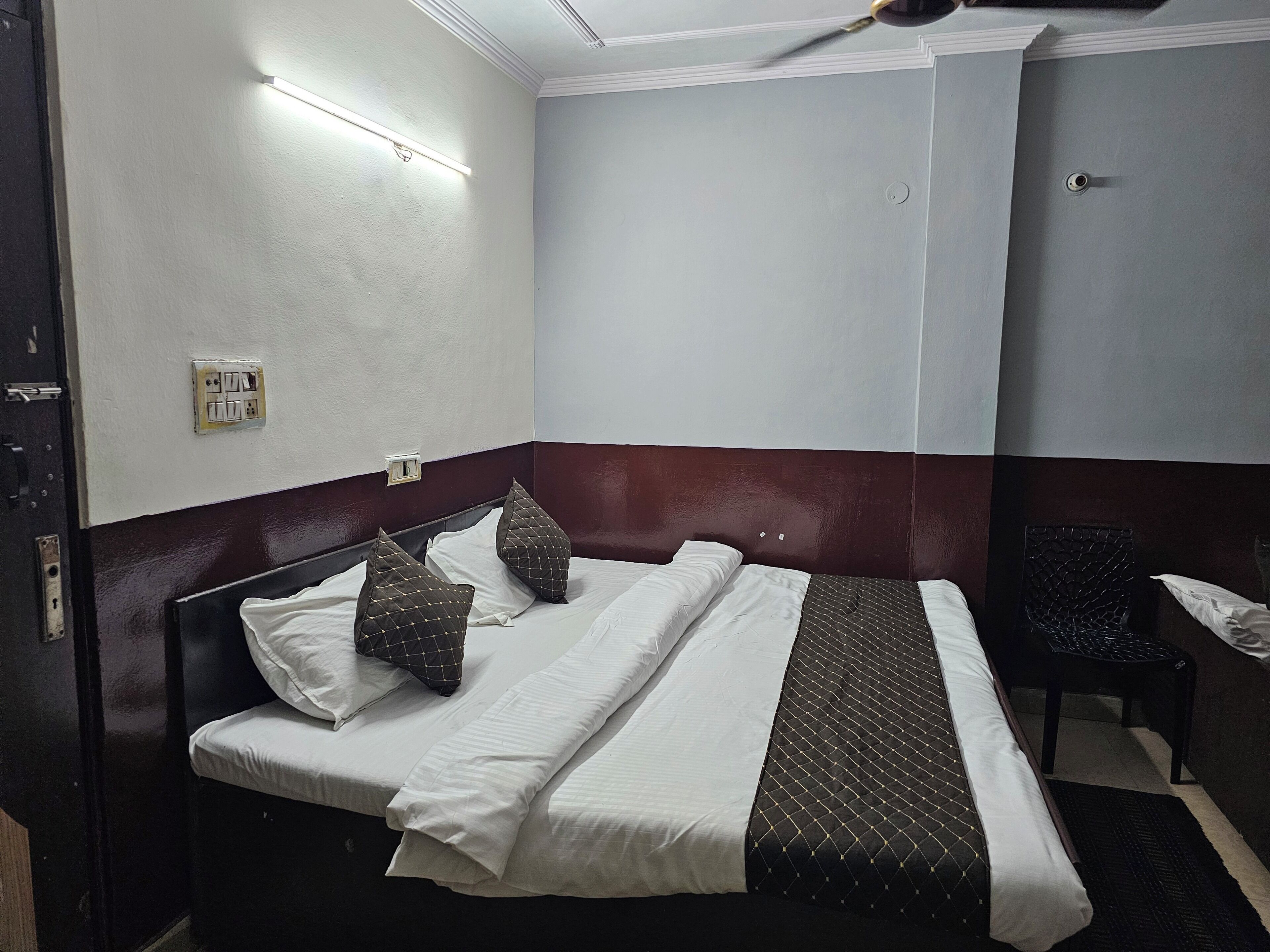 A hotel room with a bed, a chair, and a wall socket.