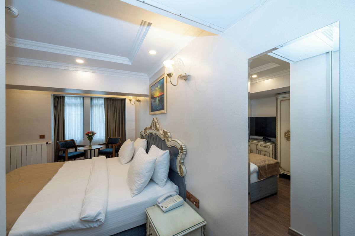 A hotel room with a large bed, a bedside table with a phone, a desk with two chairs, and a painting on the wall.