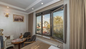 A hotel room with a bed, a desk, a chair, a small table, a lamp, and a window with a view of a mosque and cityscape. - Al Madina Hotel İstanbul (Istanbul)