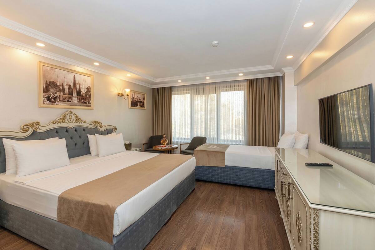 A hotel room with a large bed, a smaller bed, a desk, a chair, and a TV.