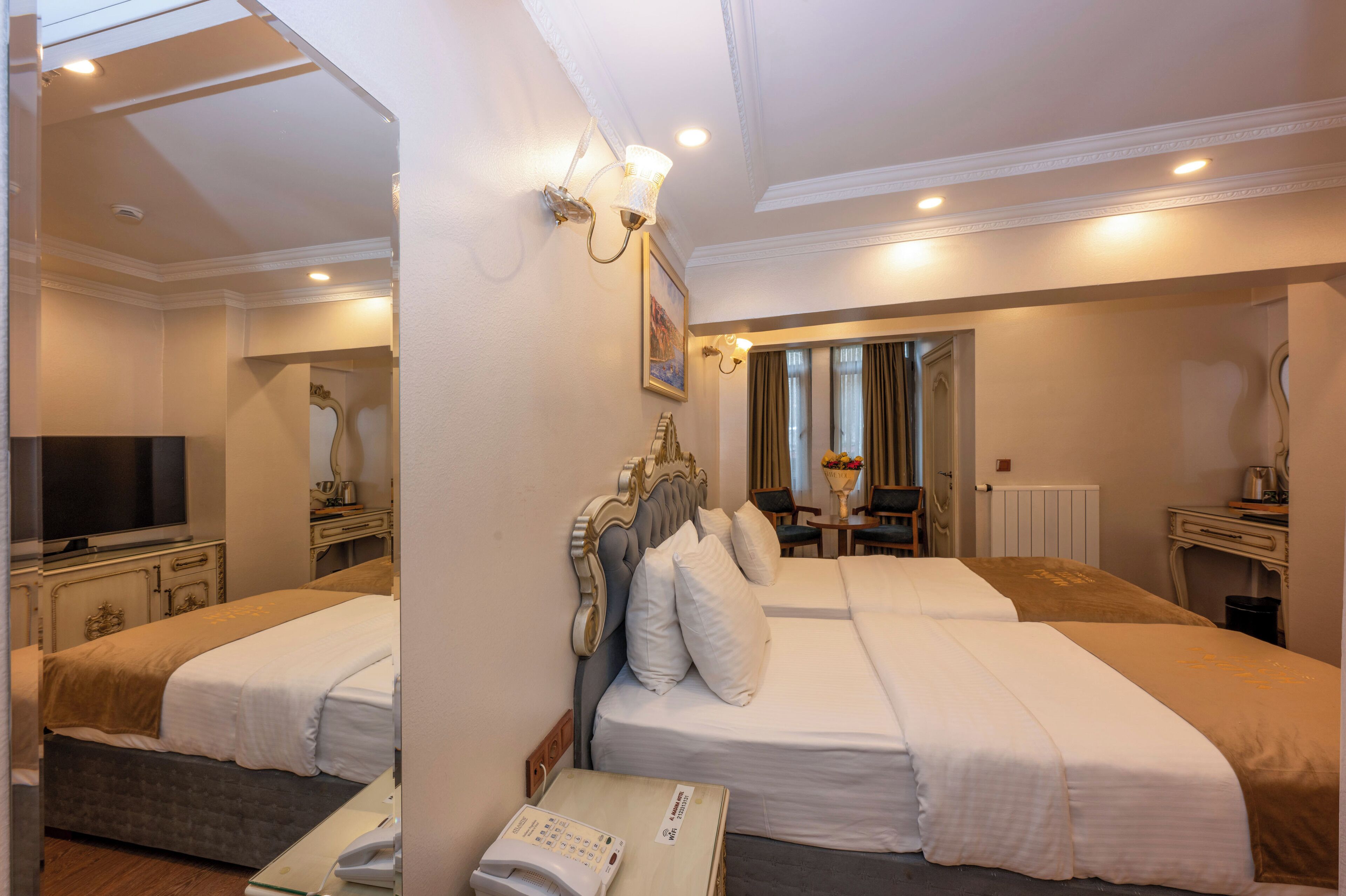 A hotel room with two beds, a television, a desk with a lamp, and a mirror.