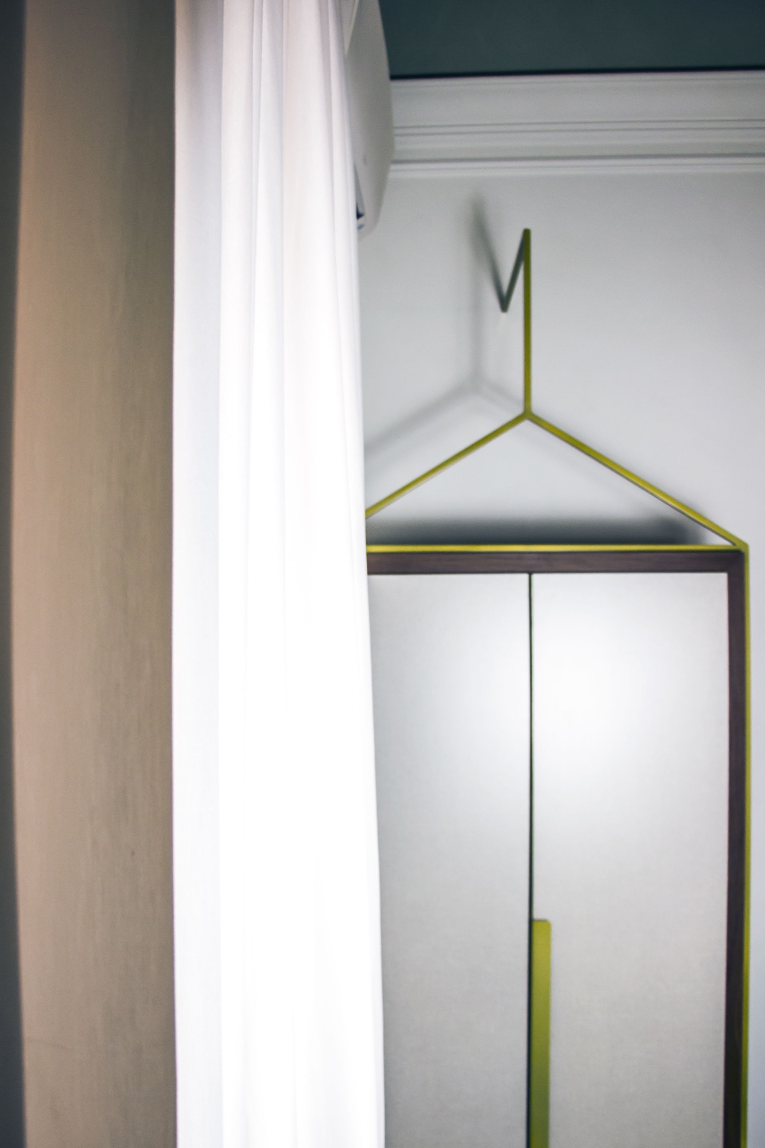 Un armadio bianco con un appendiabiti giallo e una tenda bianca che lo copre parzialmente.