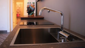 A modern kitchen with a stainless steel sink, a countertop, and a decorative sculpture in the background. - Scene Suites Apartments (Catania)