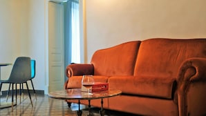 A room with a brown sofa, a small round table with a glass, and a chair. - Scene Suites Apartments (Catania)
