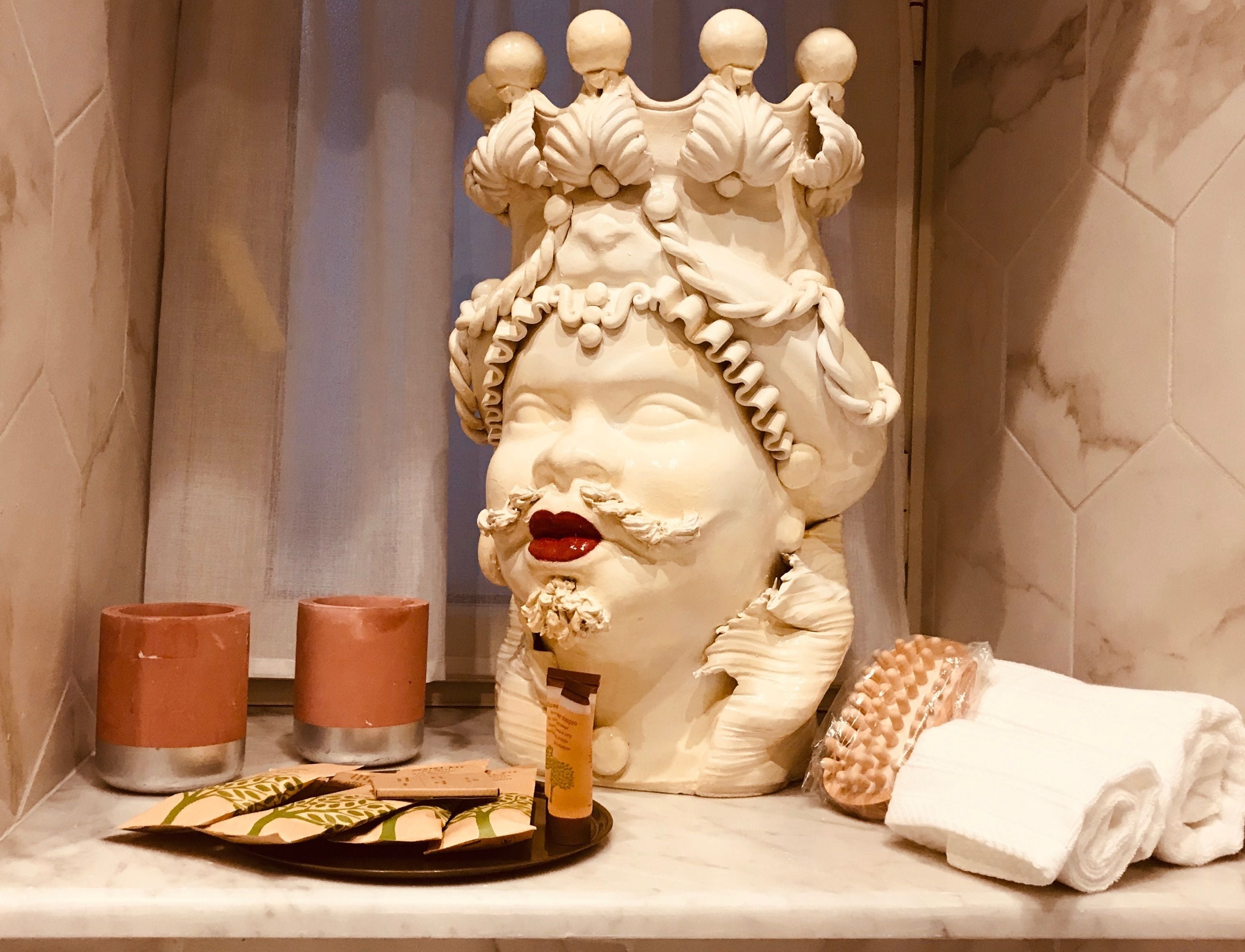 A bathroom vanity with a decorative ceramic figure, two candles, a bottle of lotion, and a towel.