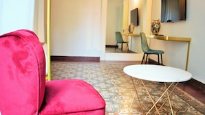 A red chair, a small white table, and a patterned floor in a room with a flat-screen TV mounted on the wall. - Scene Suites Apartments (Catania)