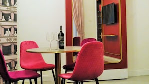 A room with a round table, two red chairs, a bottle of wine, and a mirror with a red frame. - Scene Suites Apartments (Catania)