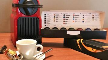 A coffee maker, a coffee pod box, a cup, and a spoon on a wooden table.