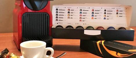 A coffee maker, a coffee pod box, a cup, and a spoon on a wooden table.