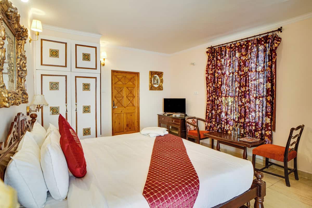 A hotel room with a large bed, a wooden desk, a television, and a wardrobe with decorative panels.