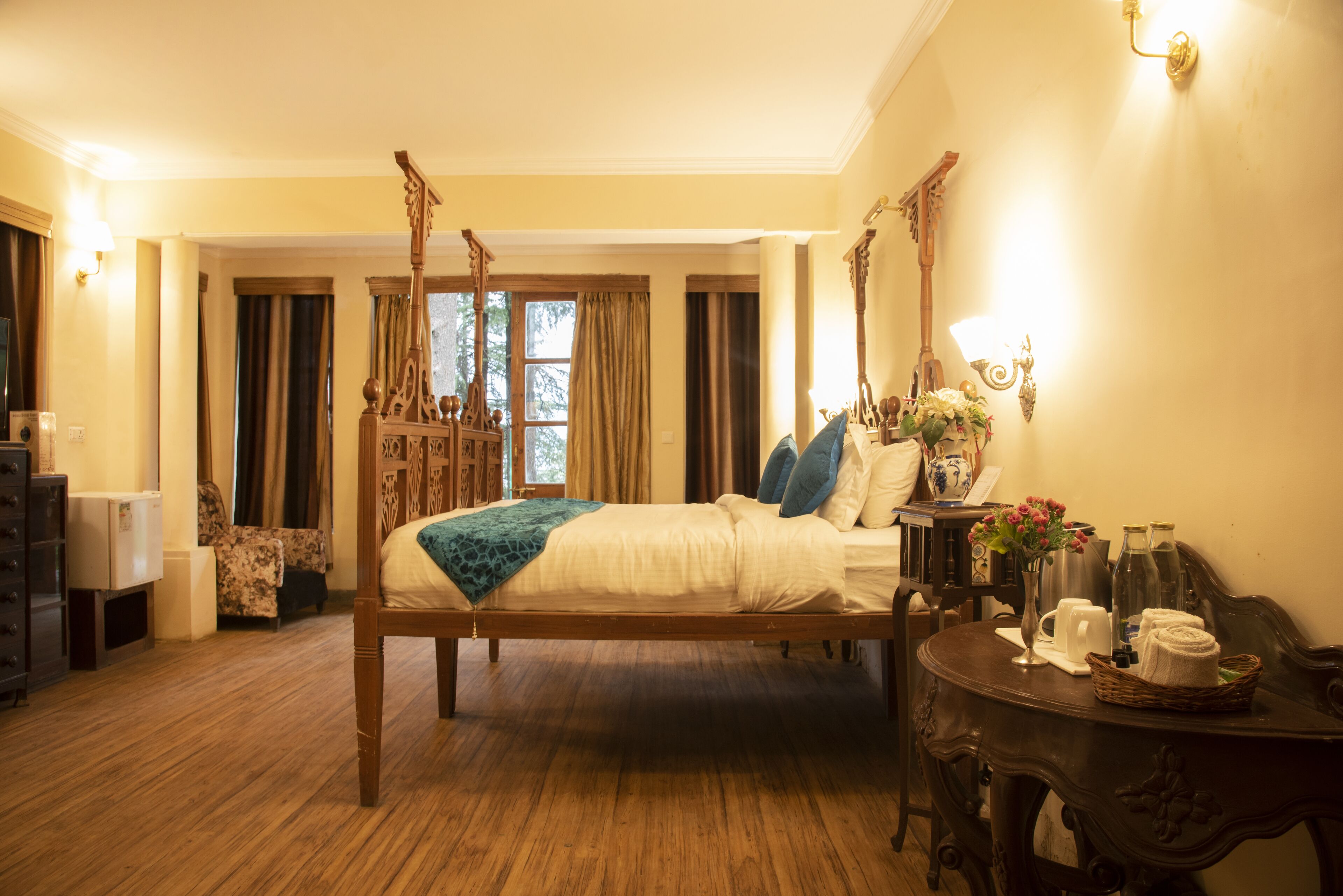 A four-poster bed with a wooden frame, a bedside table with a vase of flowers, and a small table with a basket of towels.
