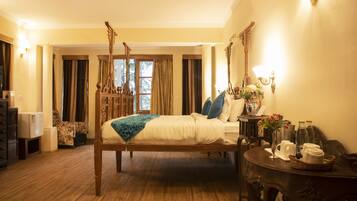 A four-poster bed with a wooden frame, a bedside table with a vase of flowers, and a small table with a basket of towels.