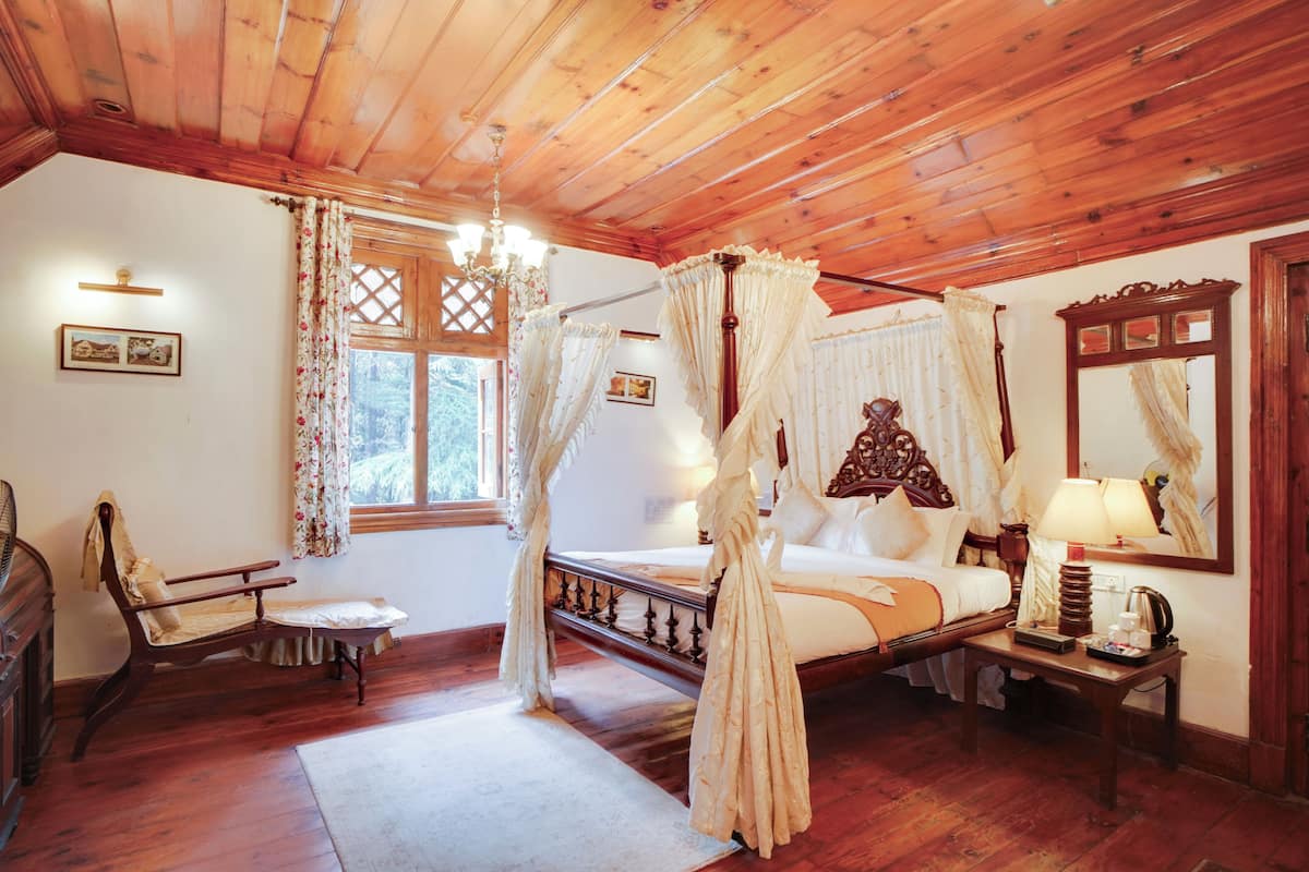 A wooden four-poster bed with a canopy, a wooden chair, a bedside table with a lamp, and a dresser.