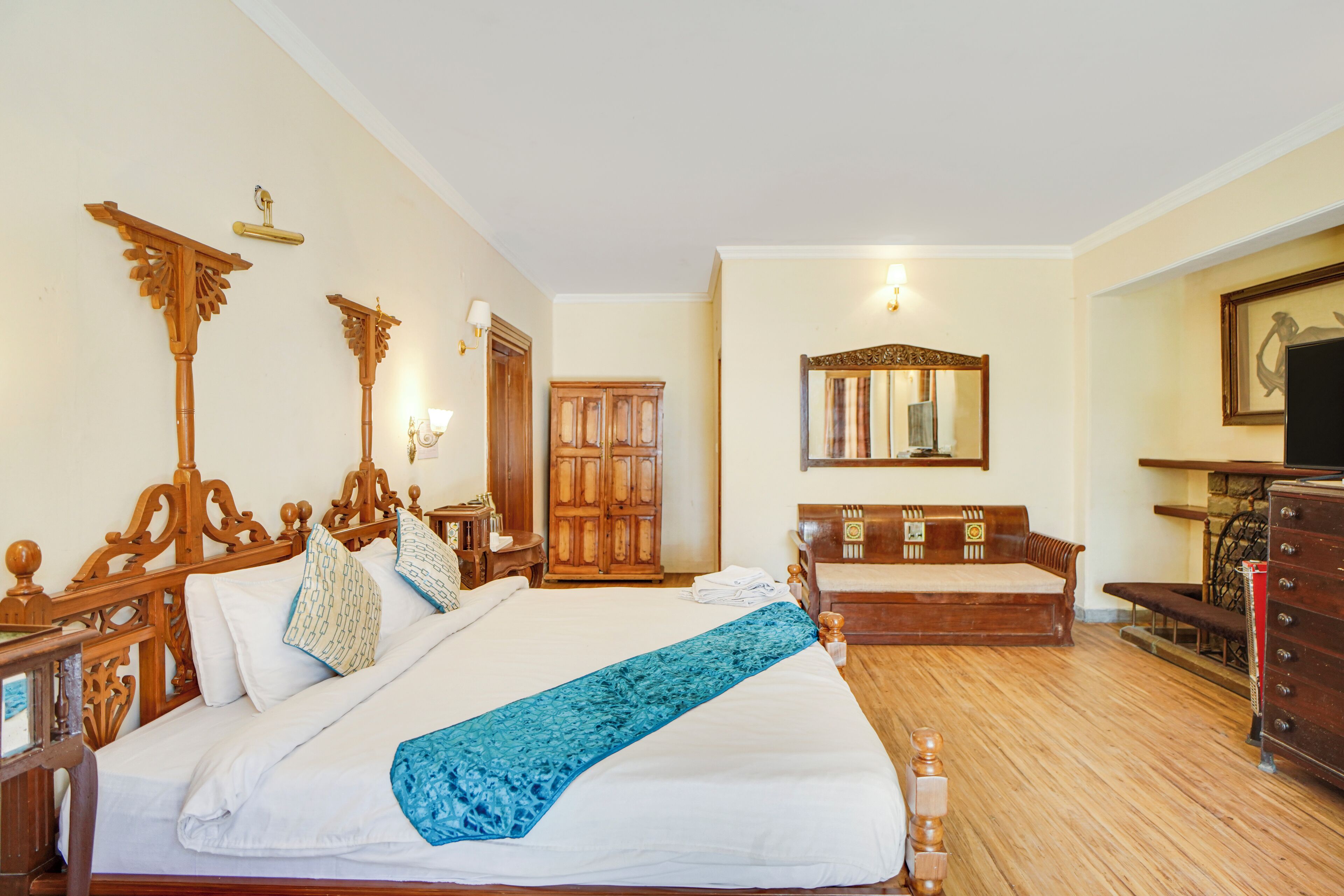 A hotel room with a large bed, wooden headboard, a wardrobe, a mirror, and a television.
