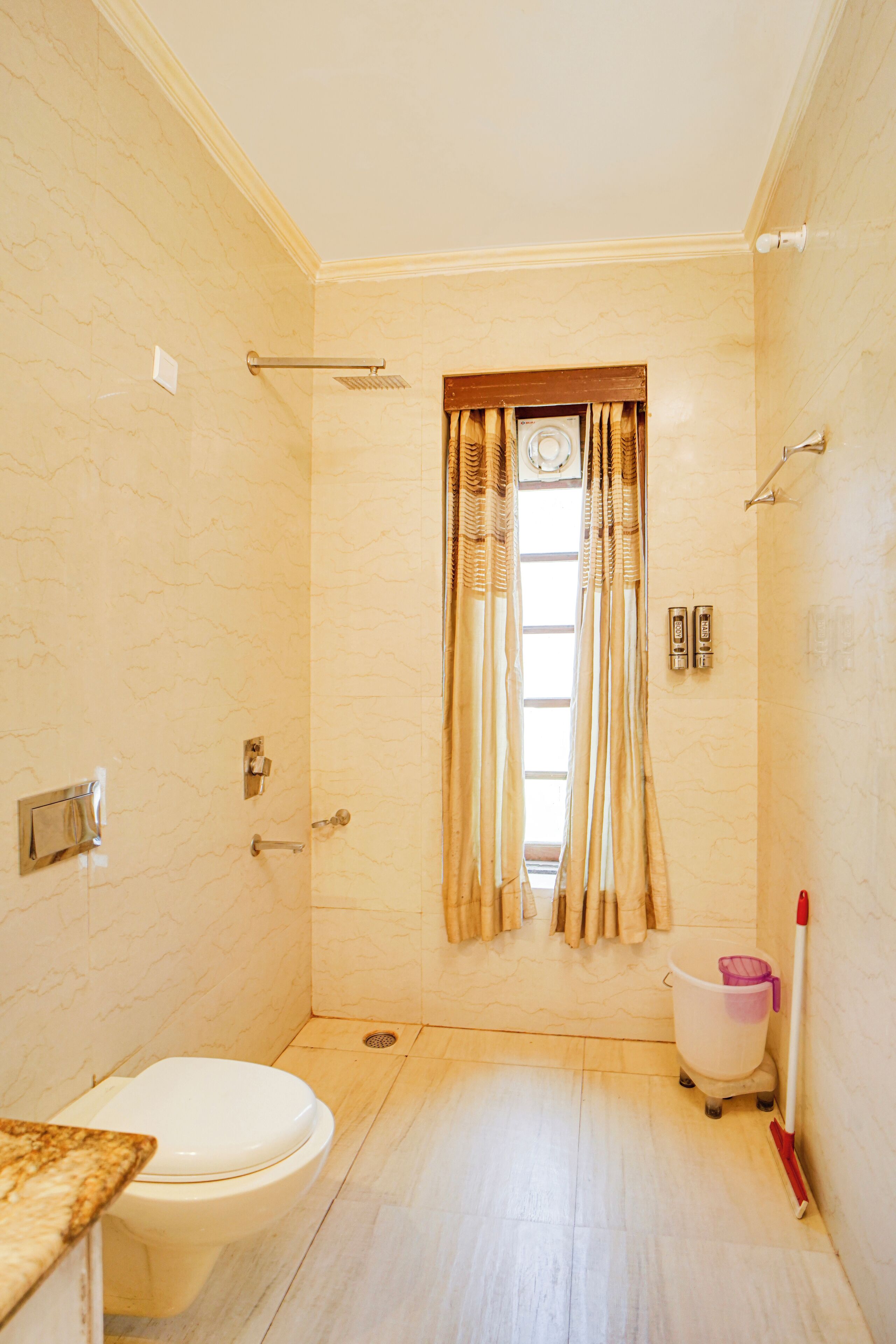 A bathroom with a toilet, a shower, and a window with curtains.