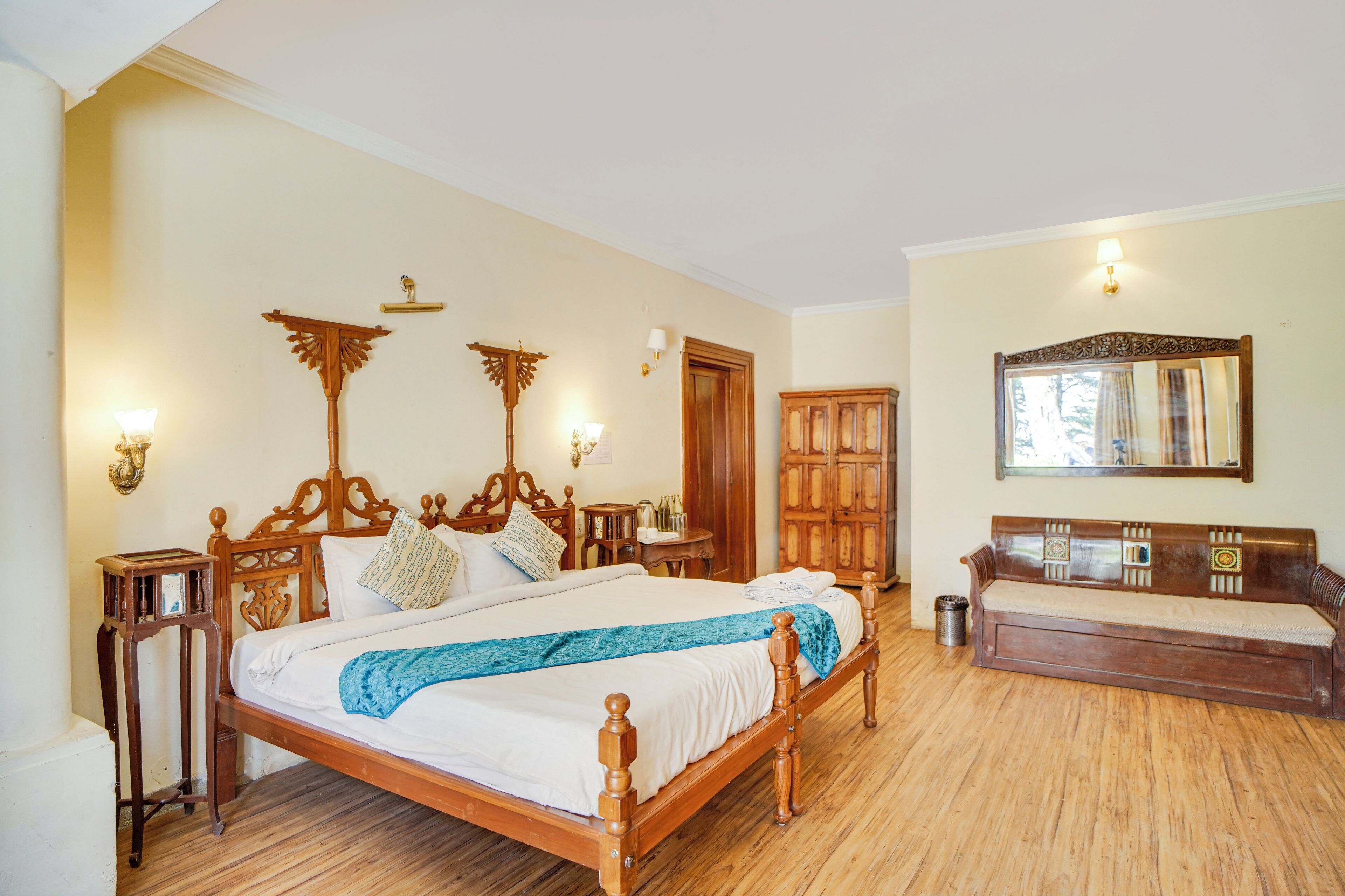 A bedroom with a wooden bed, bedside tables, a wooden bench, a wardrobe, and a mirror on the wall.